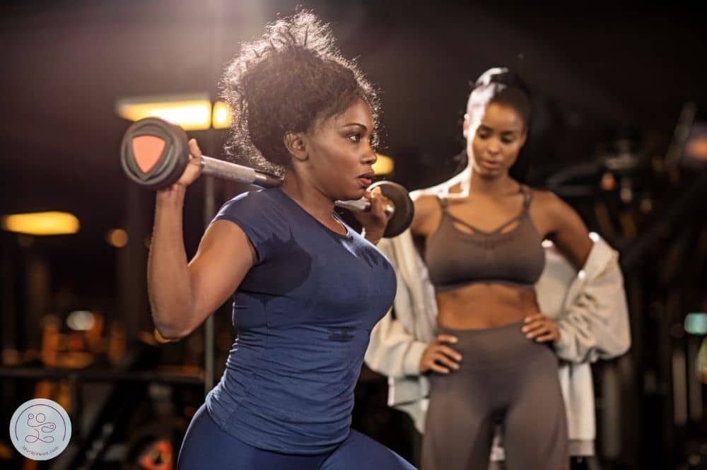 A personal trainer standing back and observing her client move.