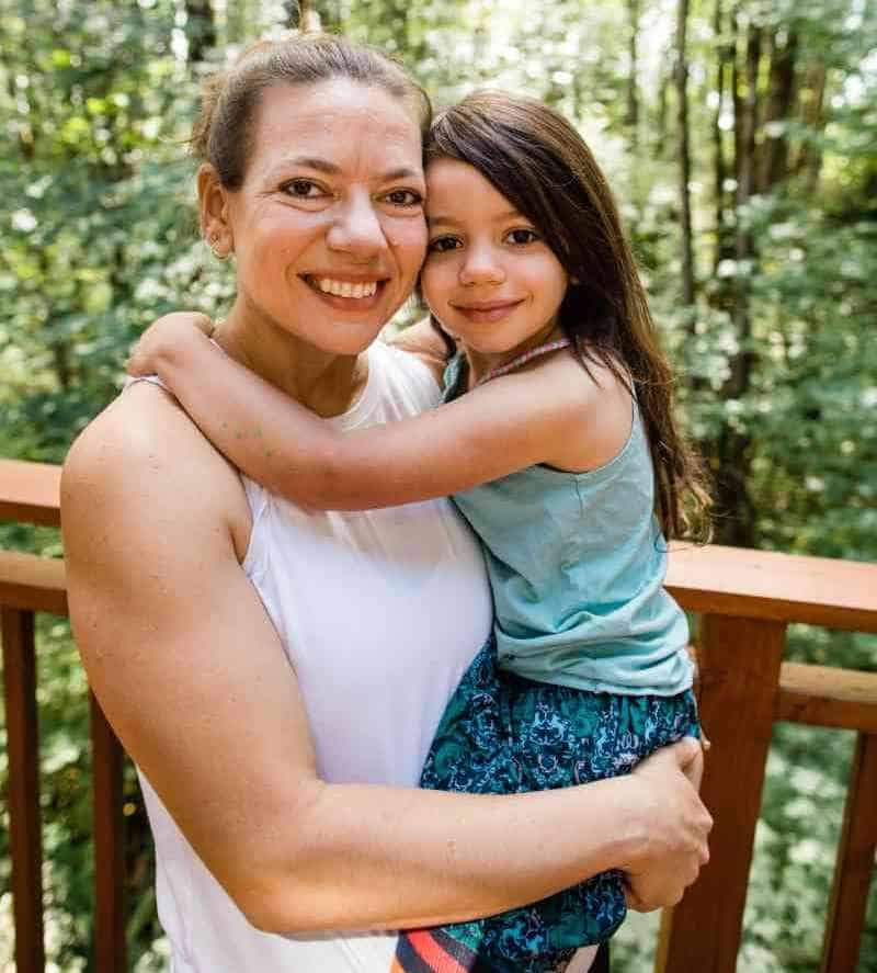 stronger-postpartum-exercise-program-2 Laura Jawad holding her daughter in front of their backyard forest.