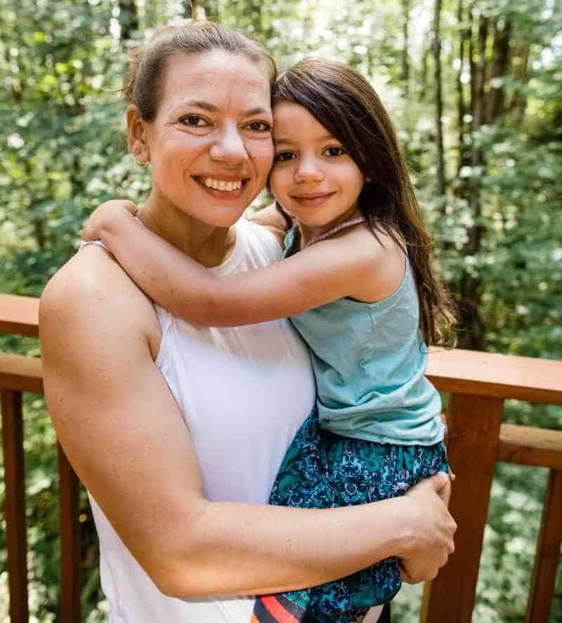 Laura Jawad holding her daughter in front of their backyard forest.